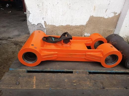 Pieza industrial metálica de color naranja con grandes aberturas cilíndricas, apoyada sobre una superficie de madera.