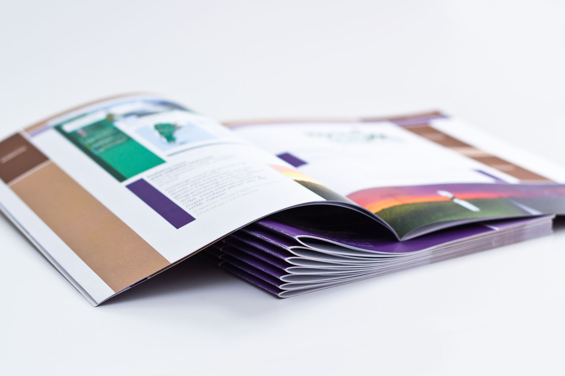 Aufgeschlagenes Magazin mit bunten Seiten, die auf einer weissen Oberfläche ausgebreitet sind