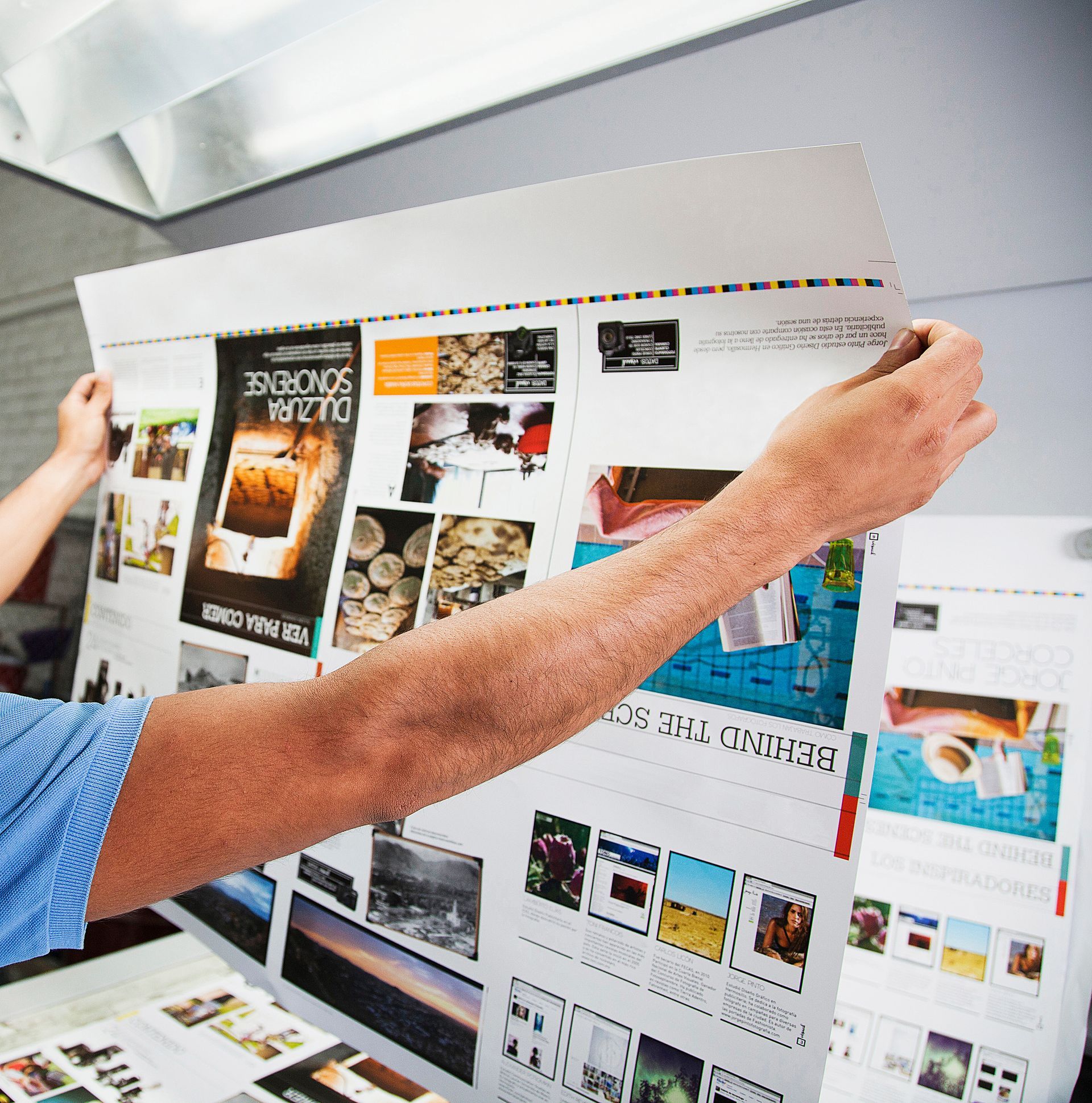 Eine Person hält während einer Designprüfung ein grosses, ausgedrucktes Webseitenlayout mit Fotos und Text hoch.