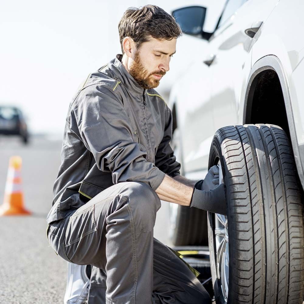 Un hombre está cambiando una llanta de un automóvil al costado de la carretera.