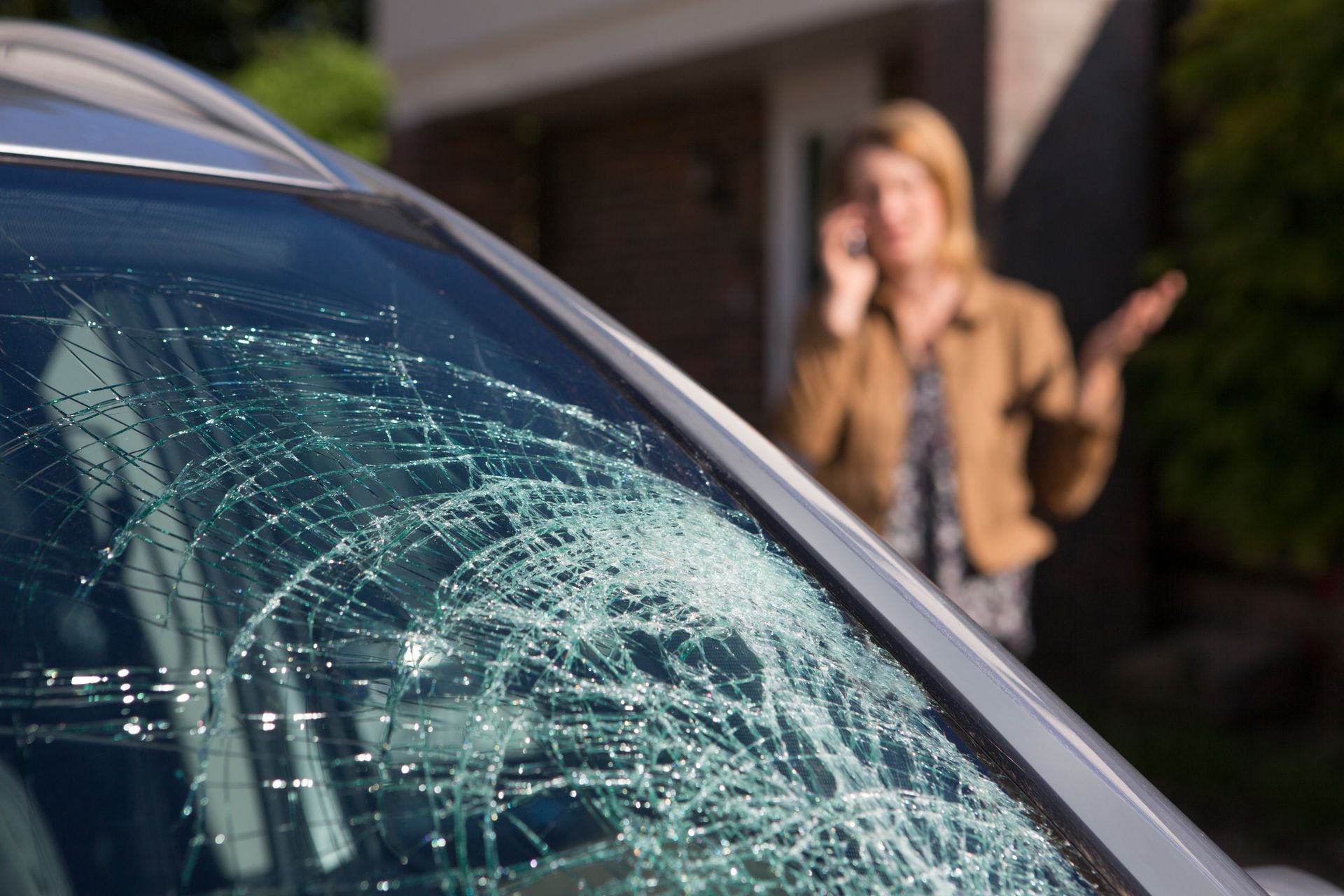 Pare-brise de voiture fissuré avec une personne floue se tenant en arrière-plan près d'une maison.