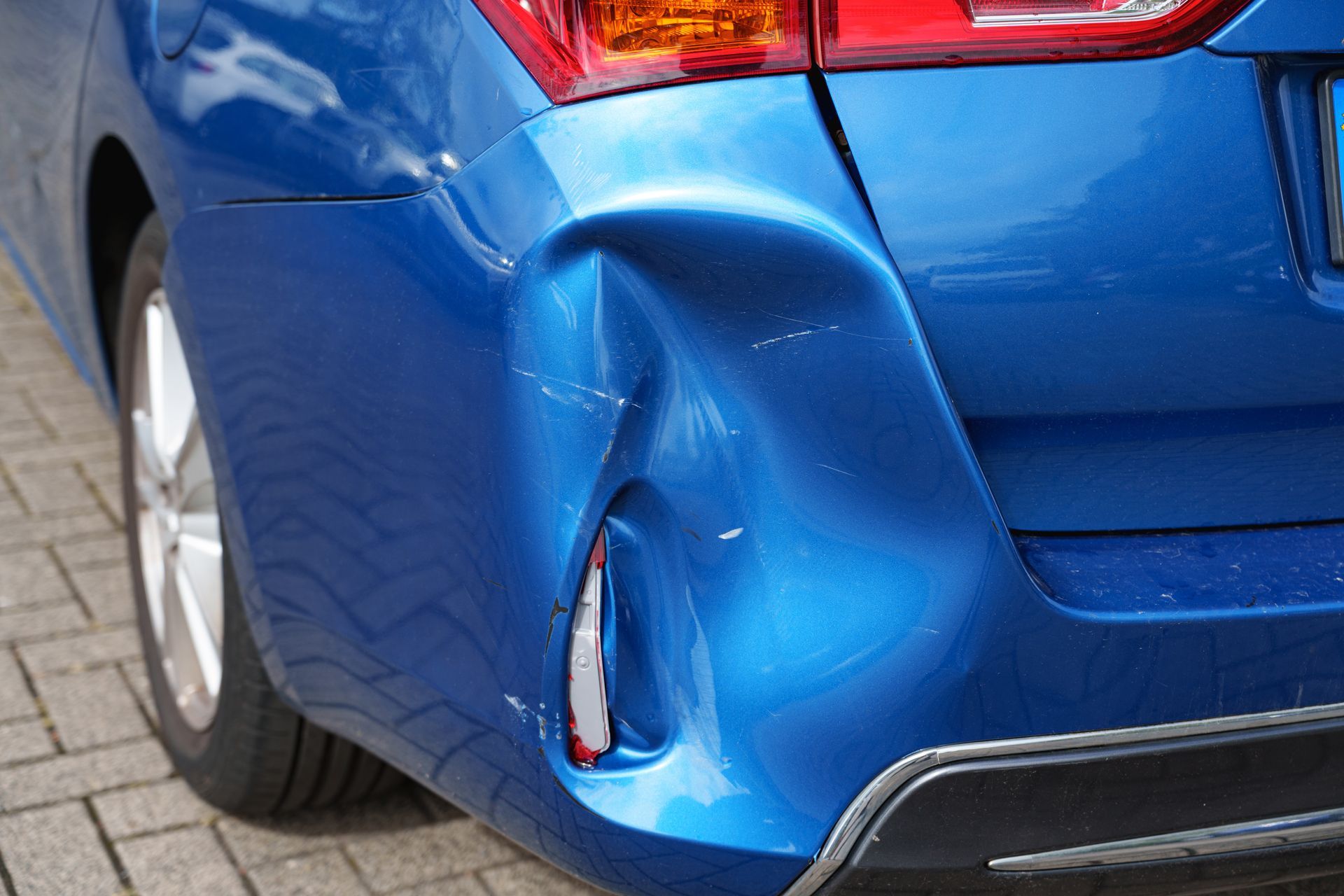 Voiture bleue avec pare-chocs arrière et feu arrière endommagés.