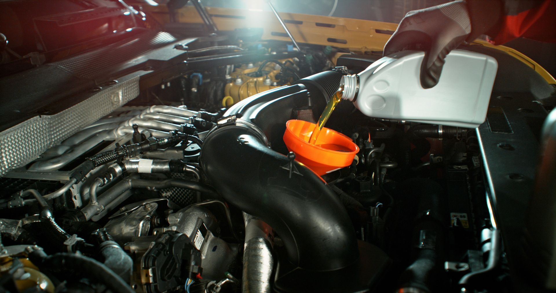 Dans le compartiment moteur d'une voiture, une main verse un liquide d'un récipient blanc dans un entonnoir orange.
