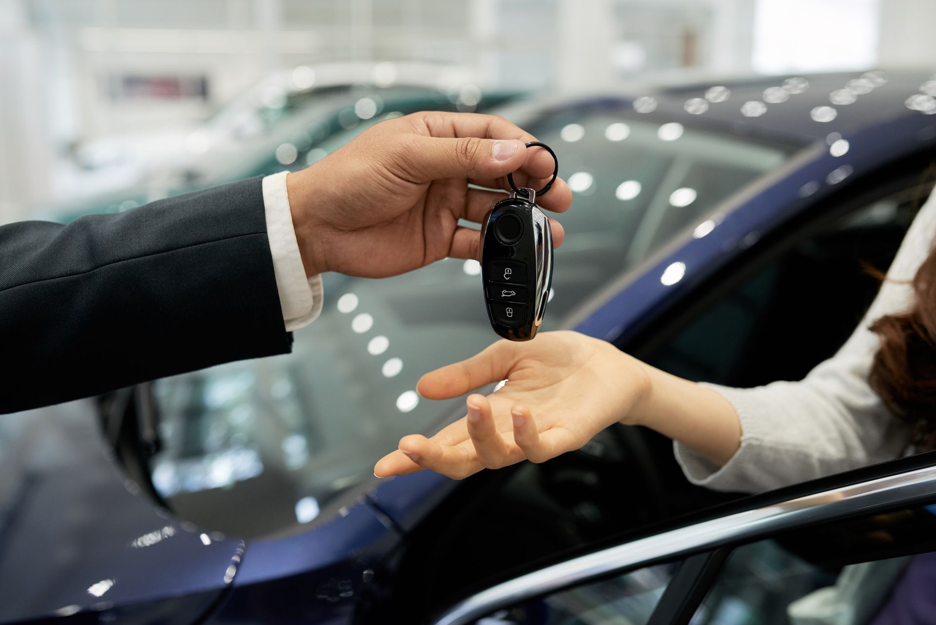 Des mains échangent des clés de voiture chez un concessionnaire, à côté d'une voiture bleu foncé.