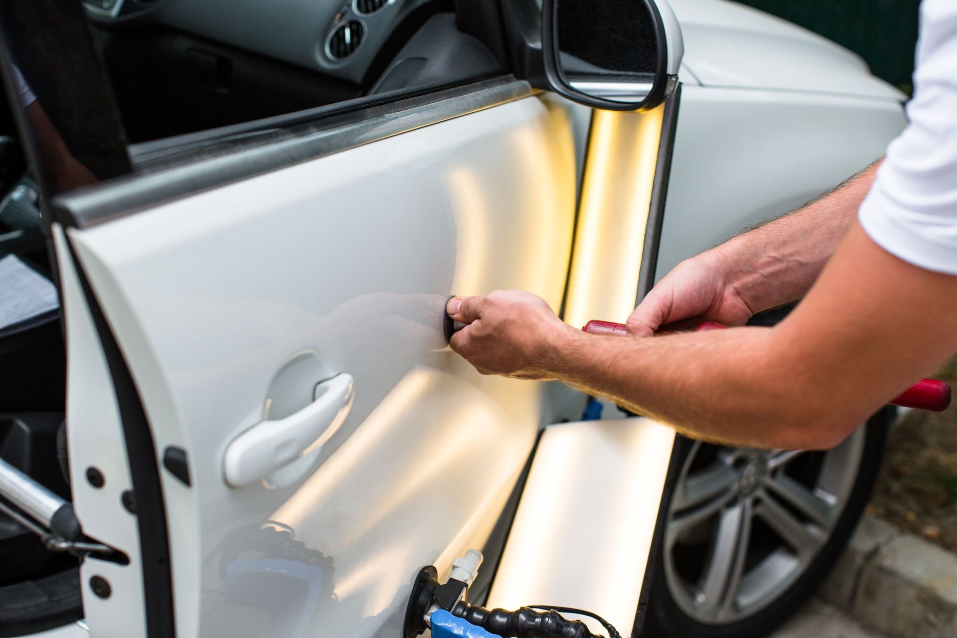 Une personne utilise une lampe de précision portative pour inspecter une portière de voiture blanche.
