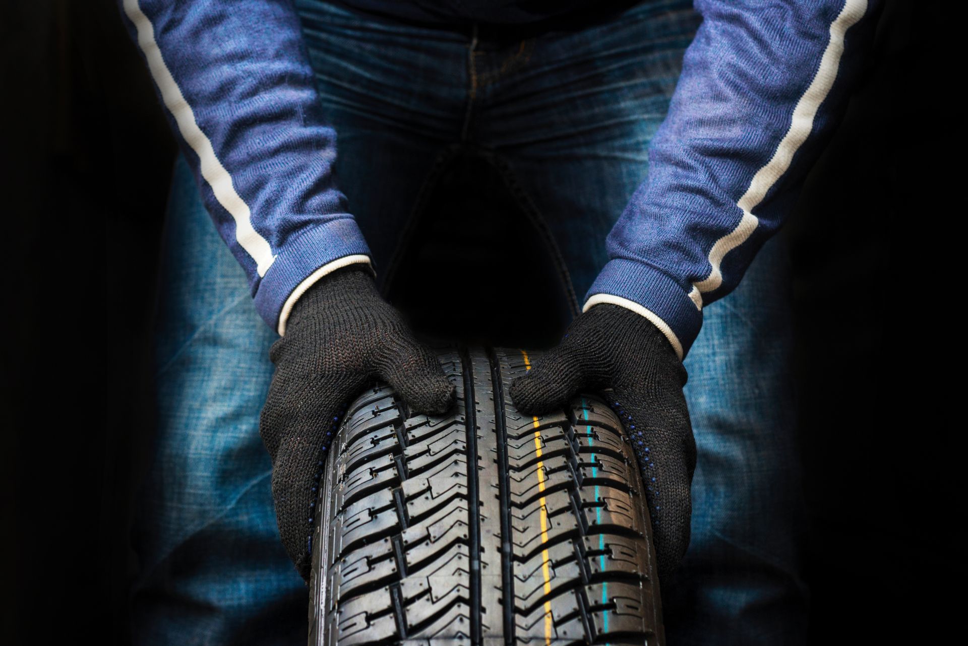 Des mains gantées tiennent un pneu de voiture dans un garage sombre.
