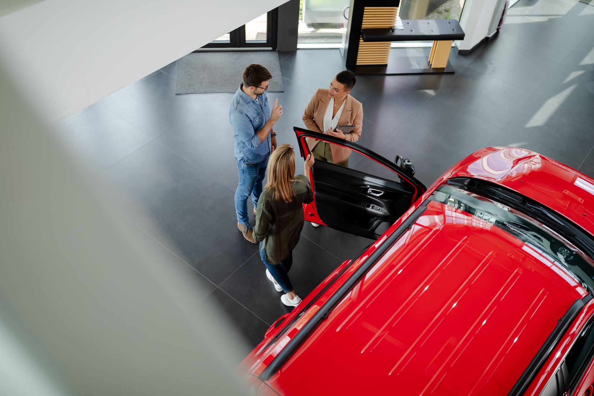 Trois personnes examinent une voiture rouge dans un showroom lumineux.