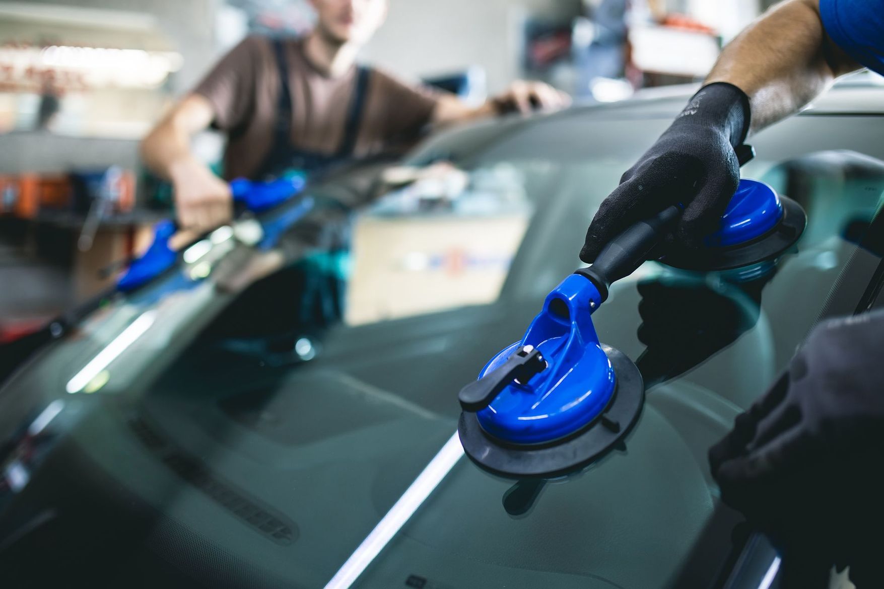 Des ouvriers changement un pare-brise de voiture avec des outils à ventouses bleus dans un atelier automobile.