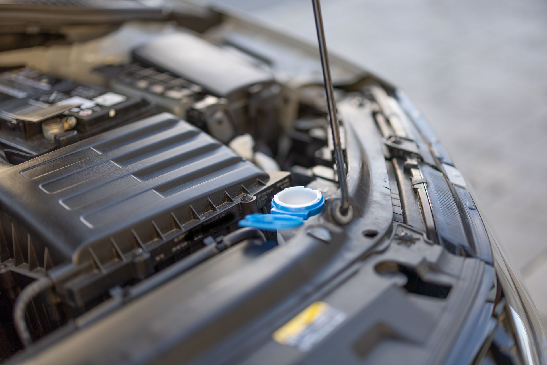 Compartiment moteur de la voiture avec capot ouvert et bouchon bleu du liquide lave-glace visible.