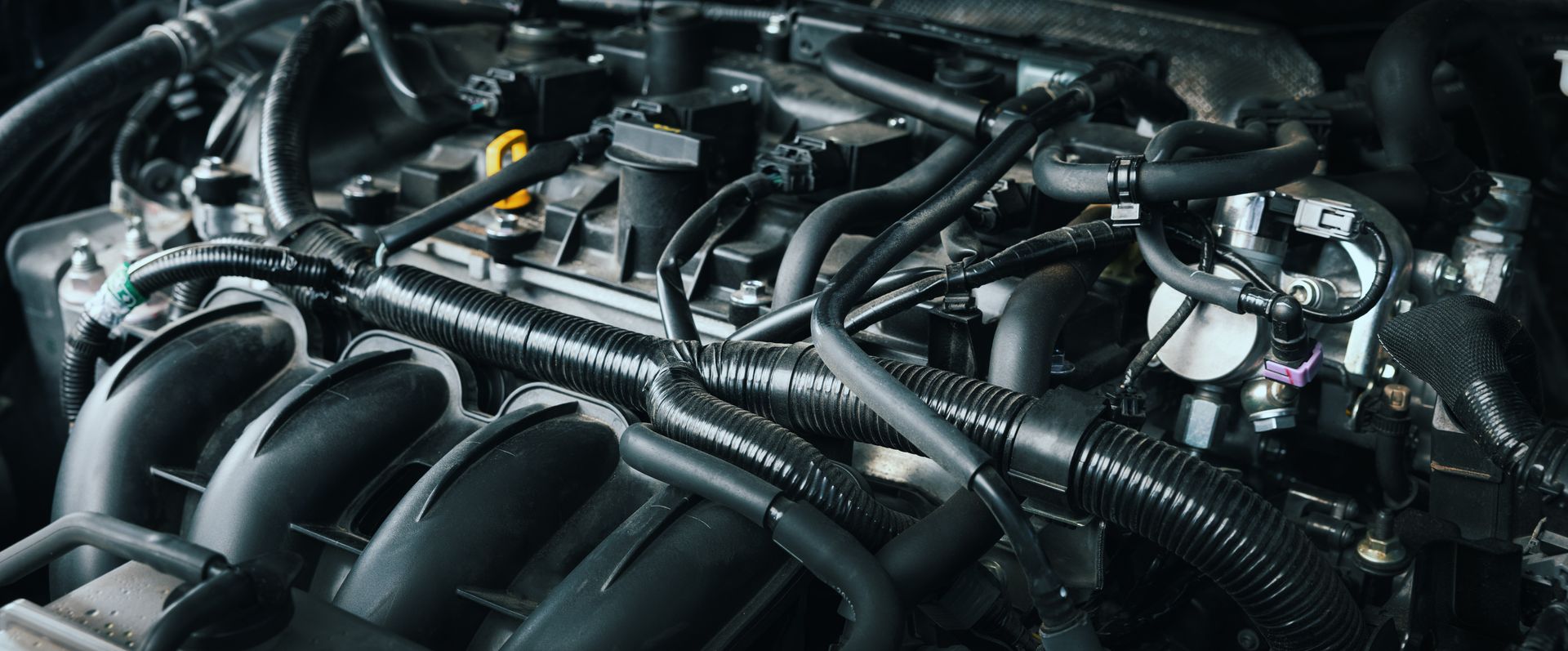 Gros plan sur le compartiment moteur d'une voiture, avec collecteur d'admission et durites noirs.