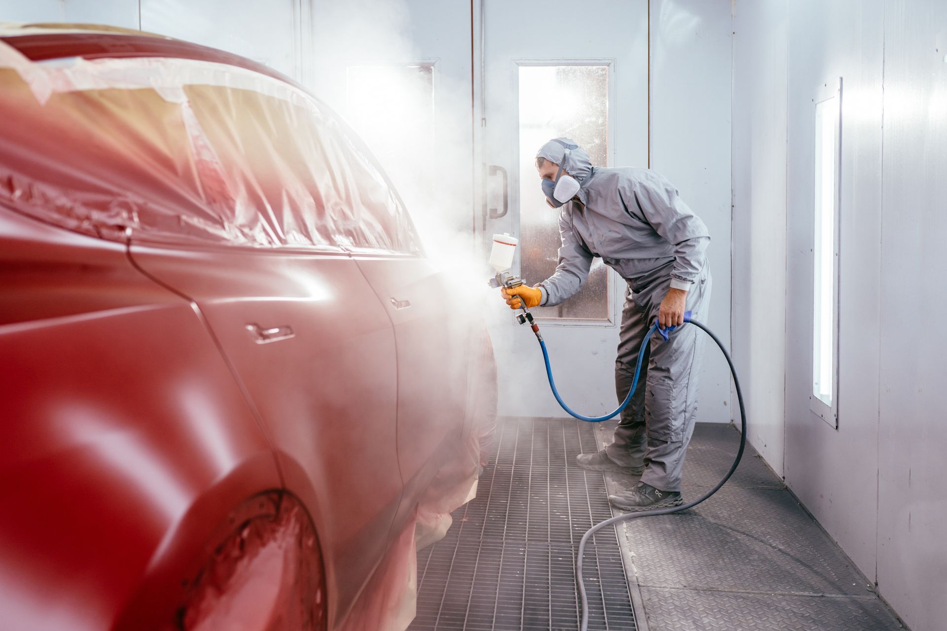 Un ouvrier peint à la bombe une voiture rouge dans un atelier de carrosserie lumineux.