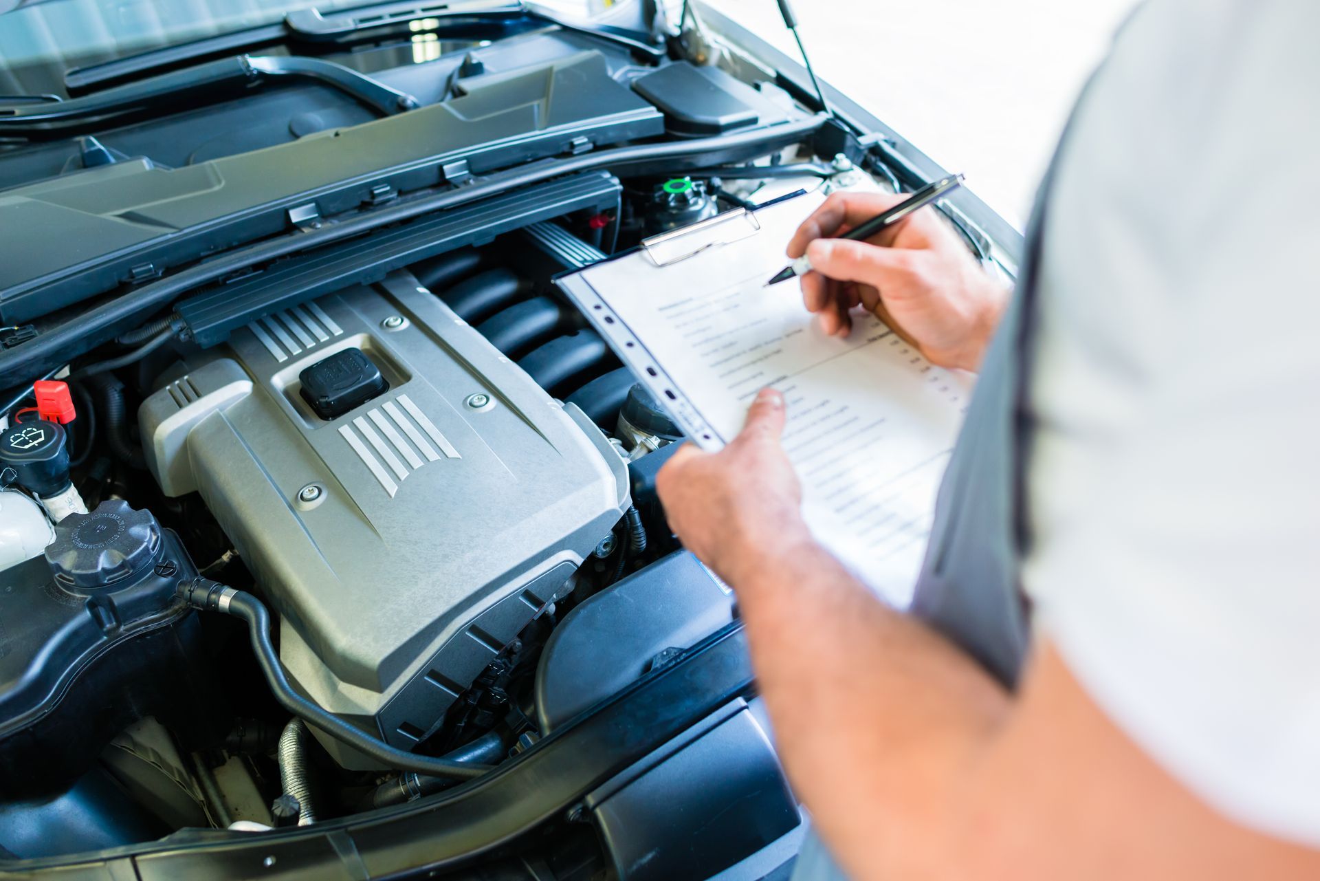 Un mécanicien inspecte le moteur d'une voiture ouverte et prend des notes sur un bloc-notes.