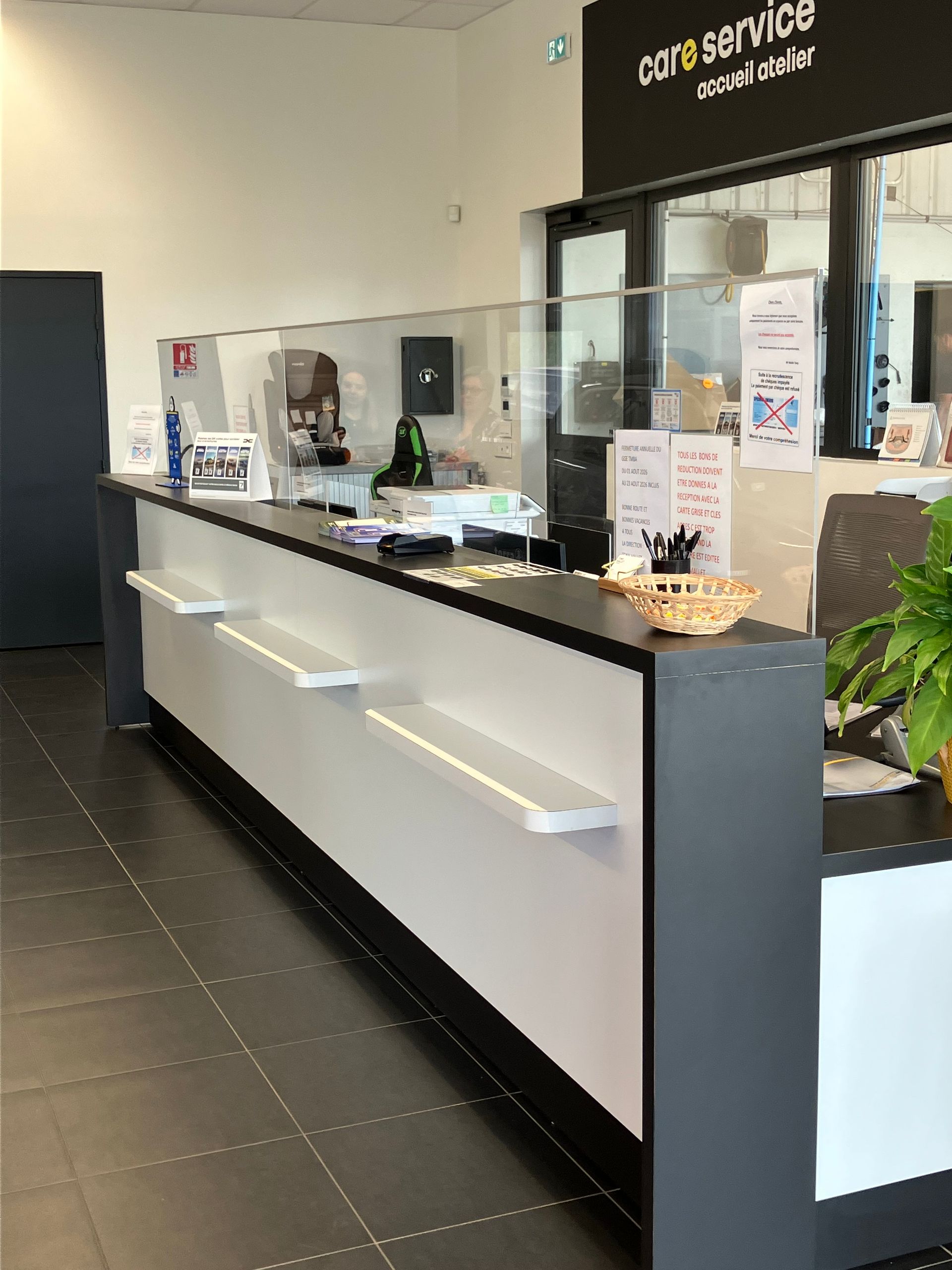 Comptoir de service dans un hall moderne avec cloisons vitrées, comptoirs blancs et sol foncé.