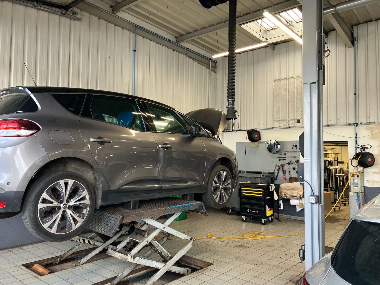 Un SUV gris est soulevé sur un pont élévateur dans un atelier de réparation automobile.