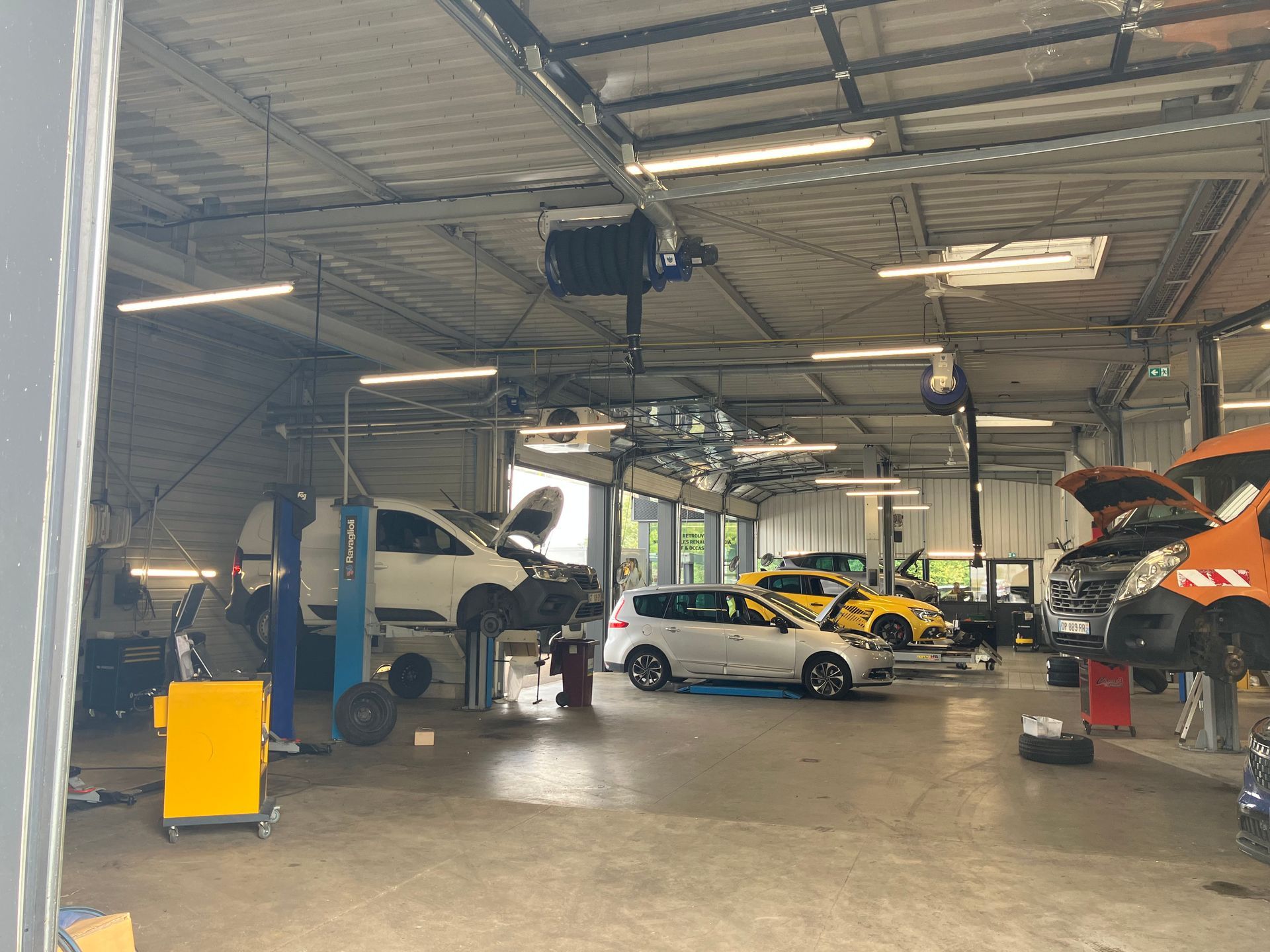 Atelier de réparation automobile avec plusieurs voitures sur des ponts élévateurs.