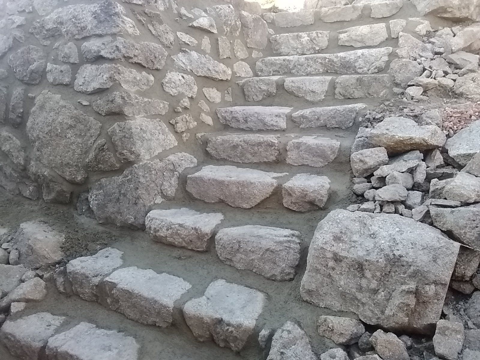 Des marches en pierre aménagées dans un mur de roche brute, au sein d'un étroit passage extérieur.