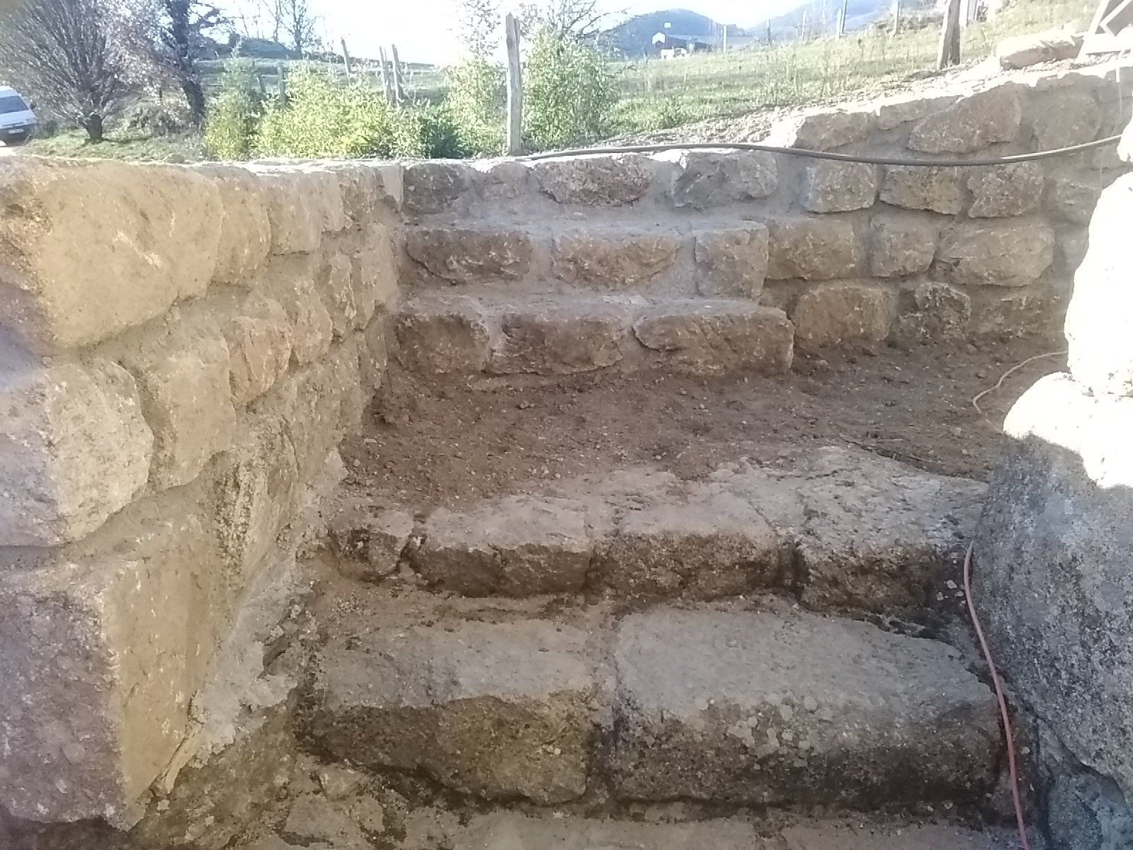 Des marches en pierre à l'extérieur, entre de bas murets de pierre, mènent au sommet d'une colline ensoleillée.
