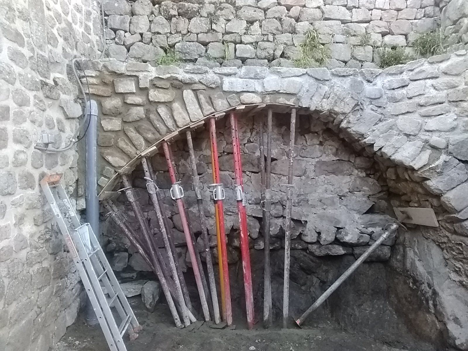 Arche en pierre avec poteaux et outils appuyés contre un mur en maçonnerie brute