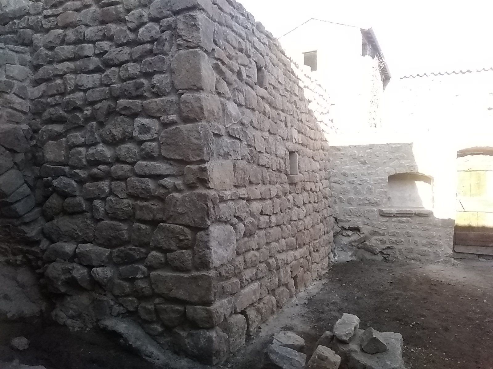 Mur de pierre dans une ruelle étroite, sol en terre battue et lumière vive du soleil en arrière-plan