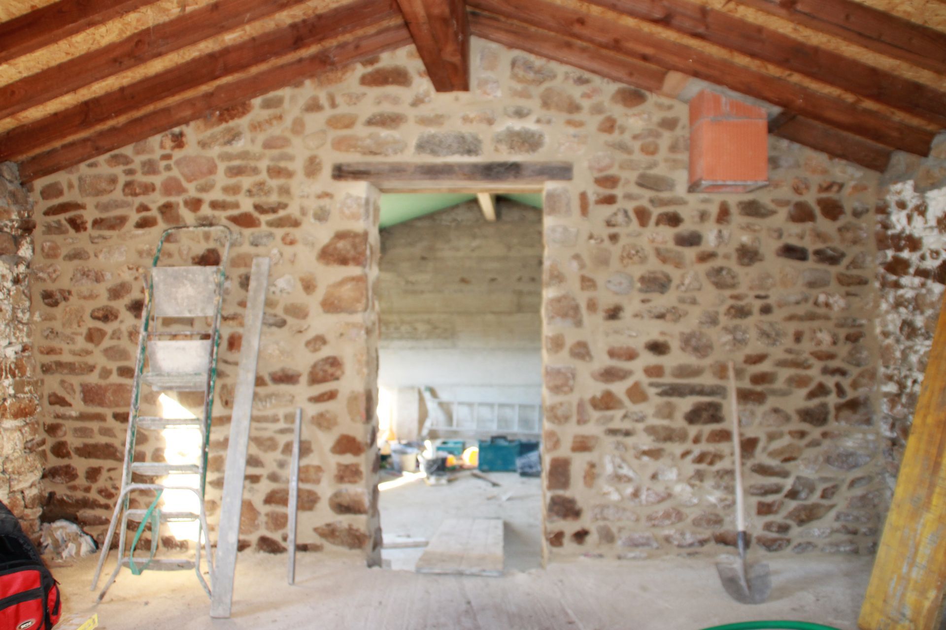 Intérieur en pierre avec porte ouverte, poutres apparentes au plafond et échelles de chaque côté.
