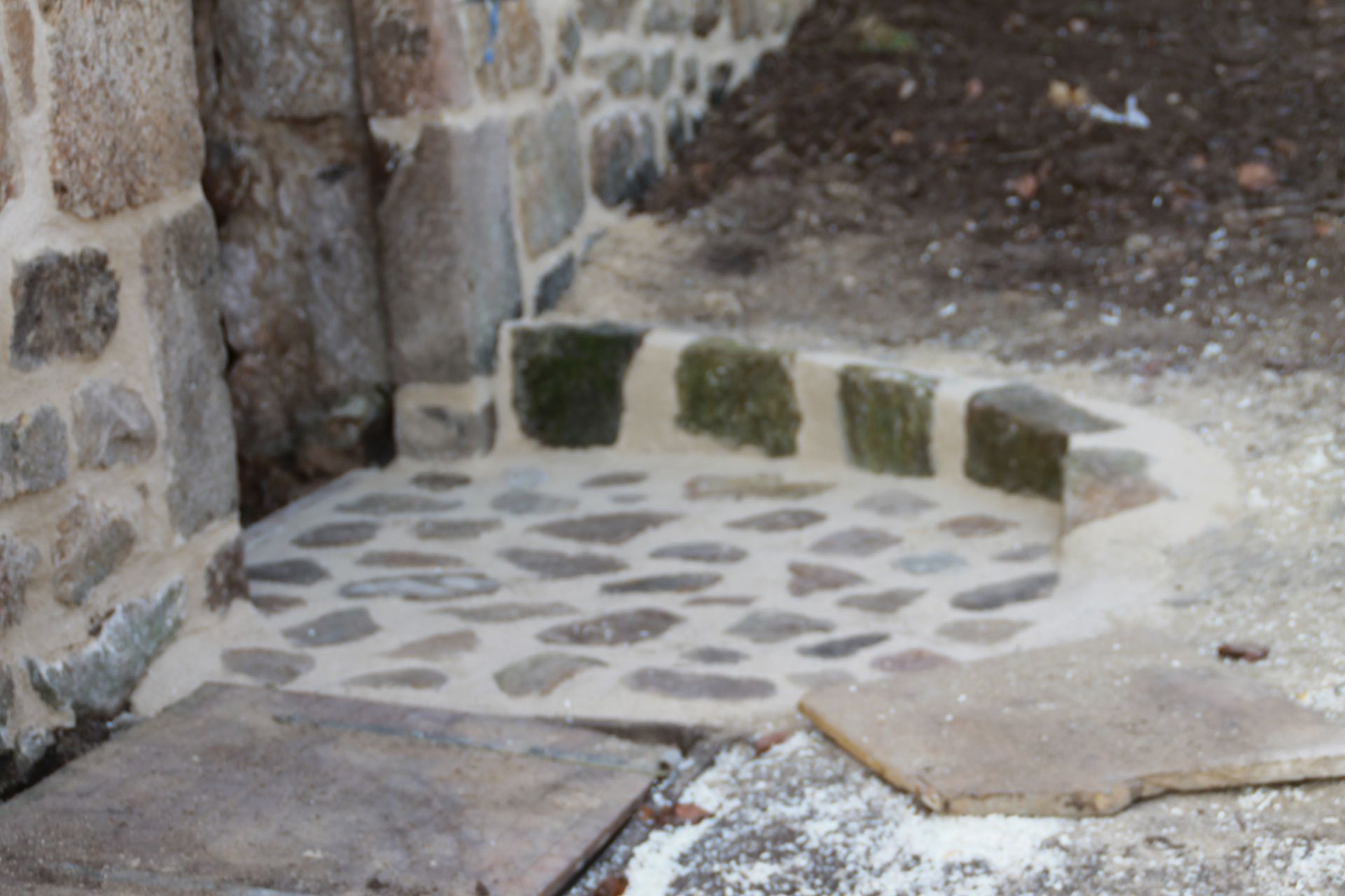 Marche en pierre ornée de pavés en mosaïque et de pierres moussues, jouxtant un mur en pierre brute