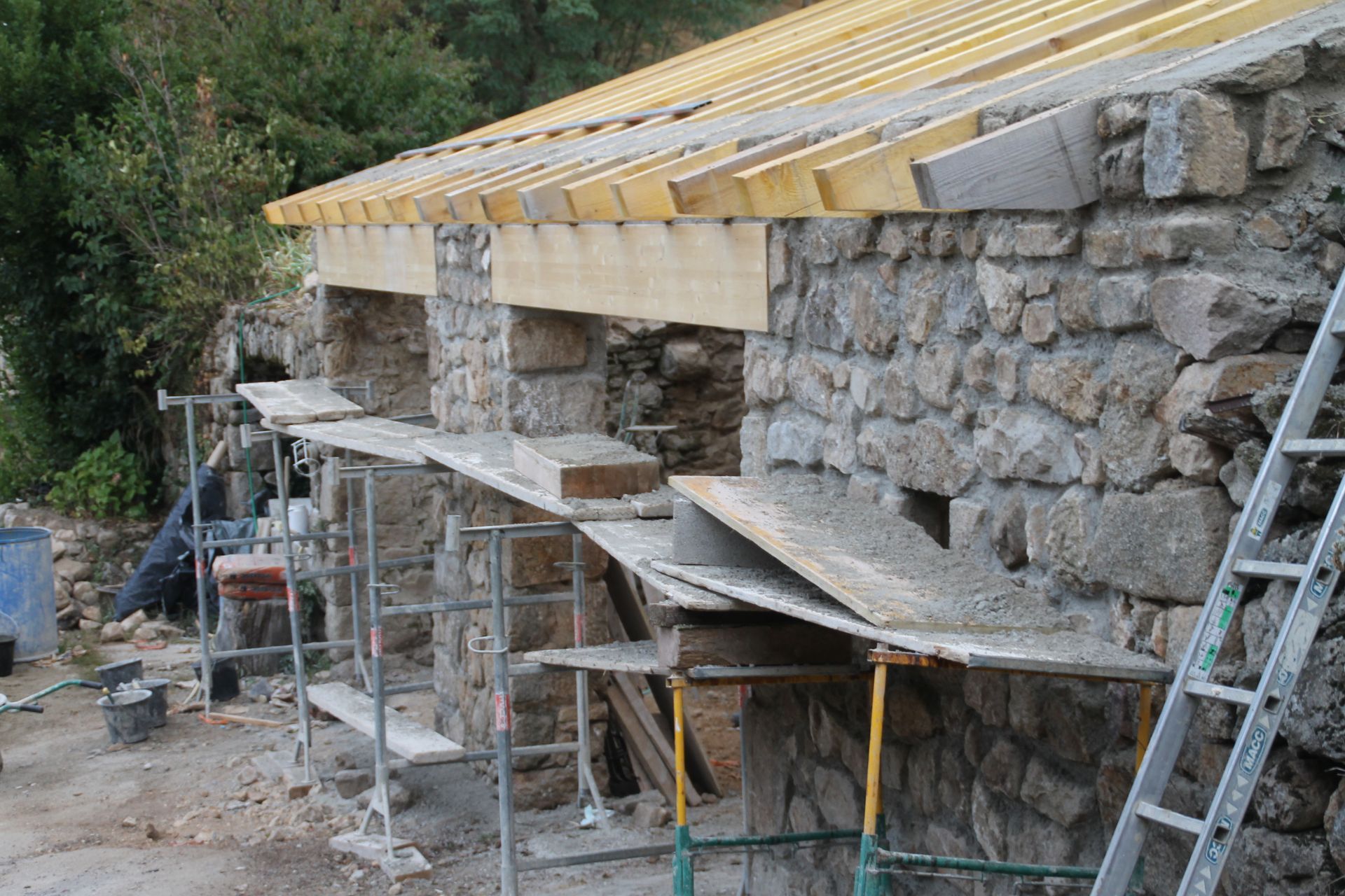 Maison en pierre en rénovation, avec des échafaudages et une échelle appuyée contre le mur.