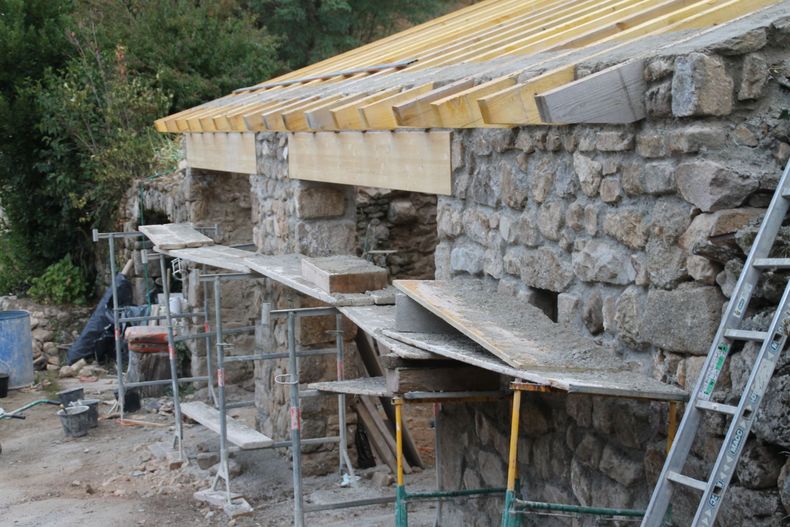 Maison en pierre en construction, avec des échafaudages et des échelles à côté d'un toit en pente