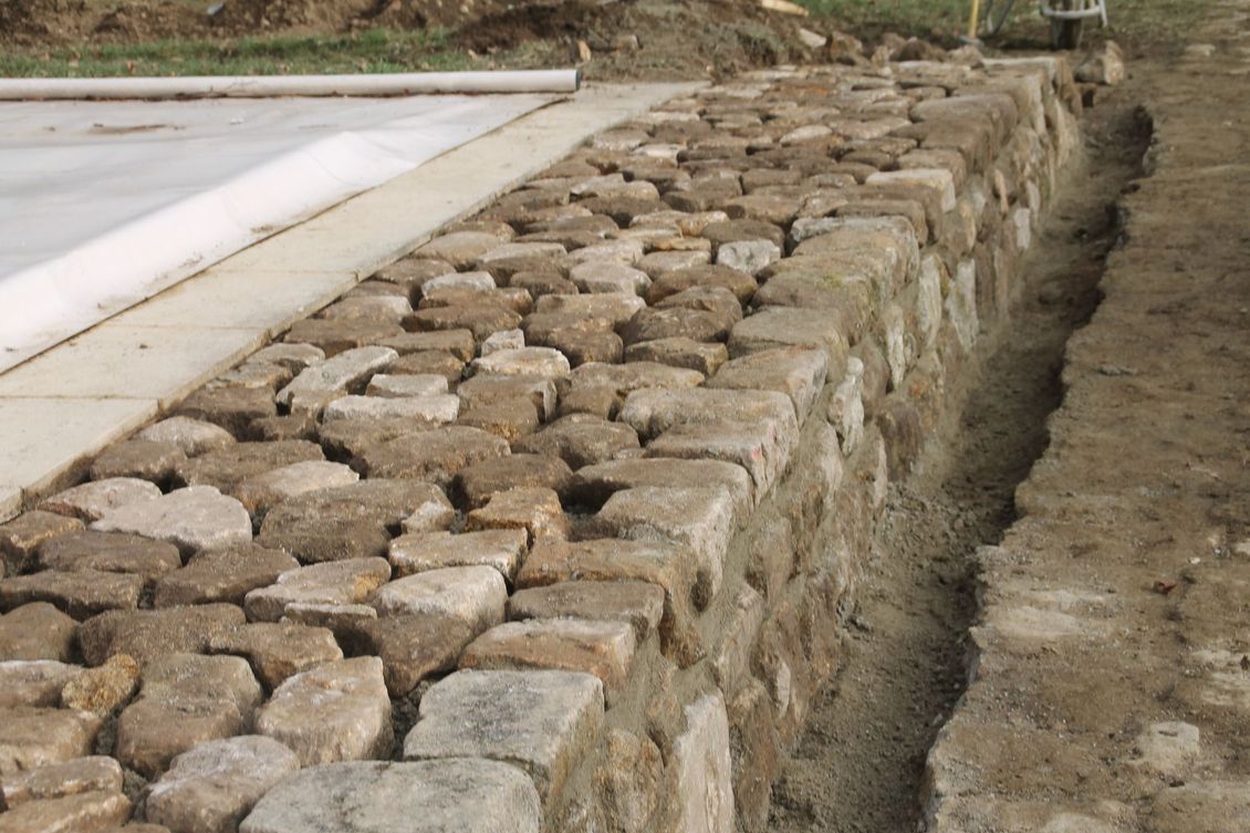 Mur de soutènement en pierre bordant une piscine et un terrain en terre battue de l'autre côté.