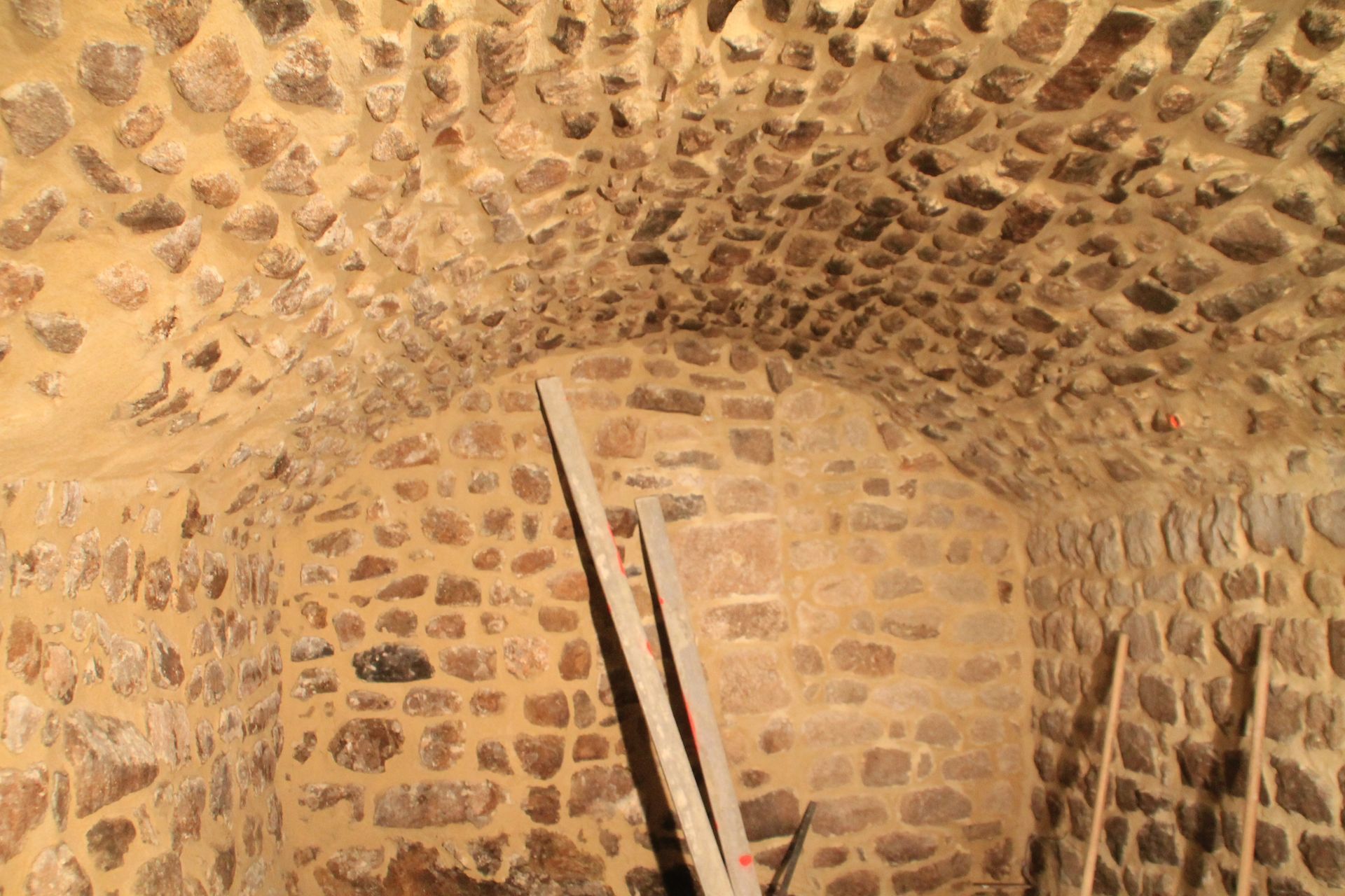 Chambre voûtée aux murs de pierre, avec plafond en arc et une échelle en bois appuyée contre le mur.