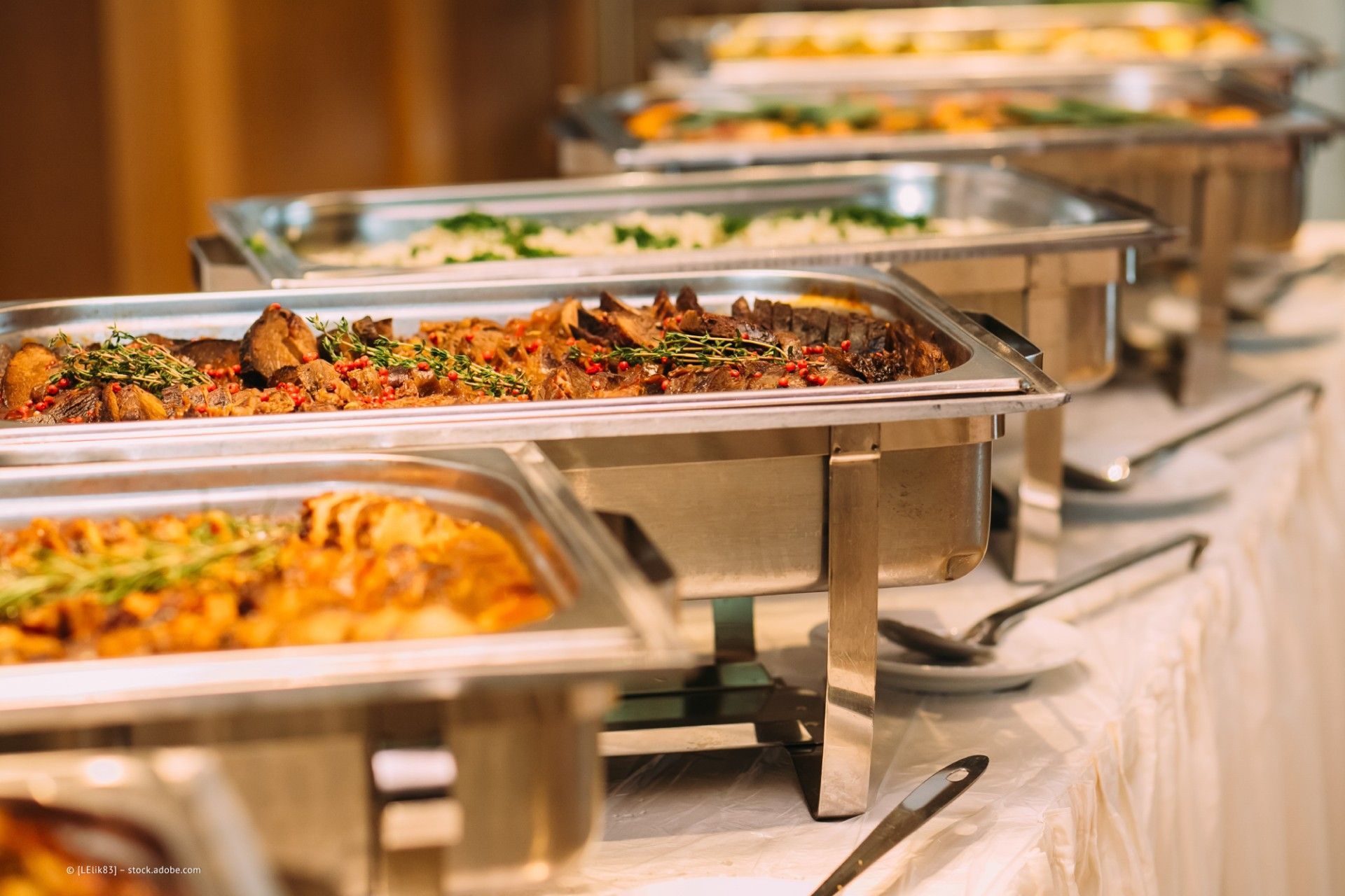 Buffet-Tabletts auf einer weißen Tischdecke mit einer Auswahl an Gerichten, die zum Servieren bei einer Veranstaltung mit Catering bereitstehen.