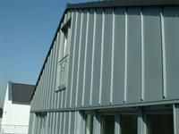 Ein graues Gebäude mit einem schwarzen Dach und vielen Fenstern.