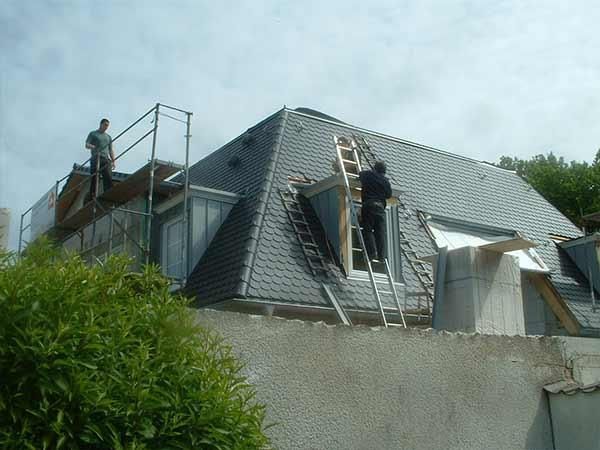 Ein Mann auf einer Leiter arbeitet auf dem Dach eines Gebäudes.