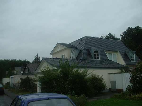 Ein blaues Auto parkt vor einem großen weißen Haus mit grauem Dach.