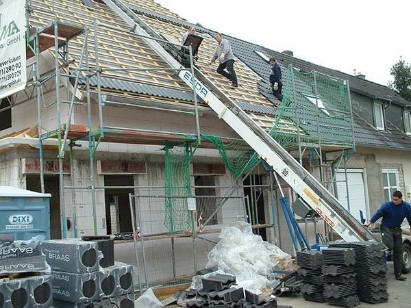 Ein Mann trägt einen Stapel Ziegel vor einem im Bau befindlichen Gebäude