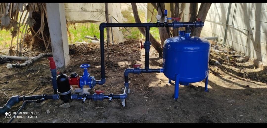 Un tanque azul está sentado sobre un campo de tierra al lado de un árbol.