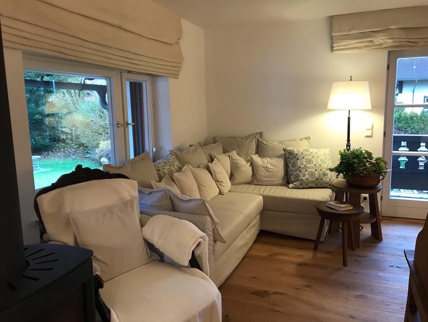 Wohnzimmer mit cremefarbenem Ecksofa, Sessel und Holzboden. Großes Fenster mit Blick ins Freie.