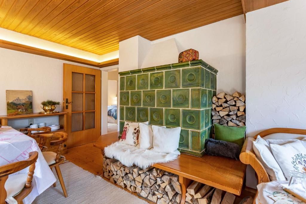 Gemütliches Interieur mit grünem Kachelofen, Holzbank und Brennholz. Holzdecke, -tür und -tisch.