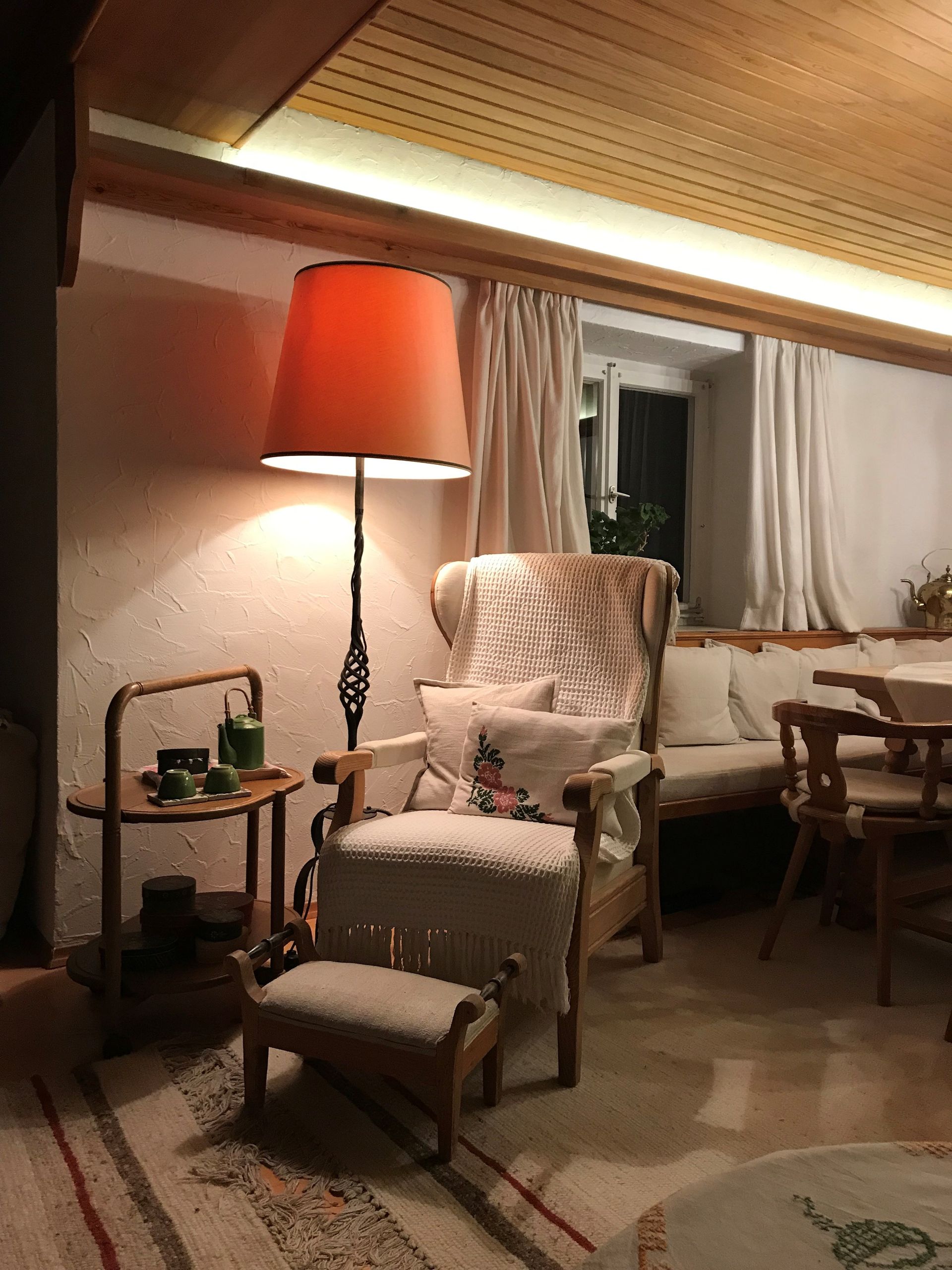 Gemütliches Wohnzimmer mit orangefarbenem Lampenschirm, Sessel, Hocker und kleinem Beistelltisch.