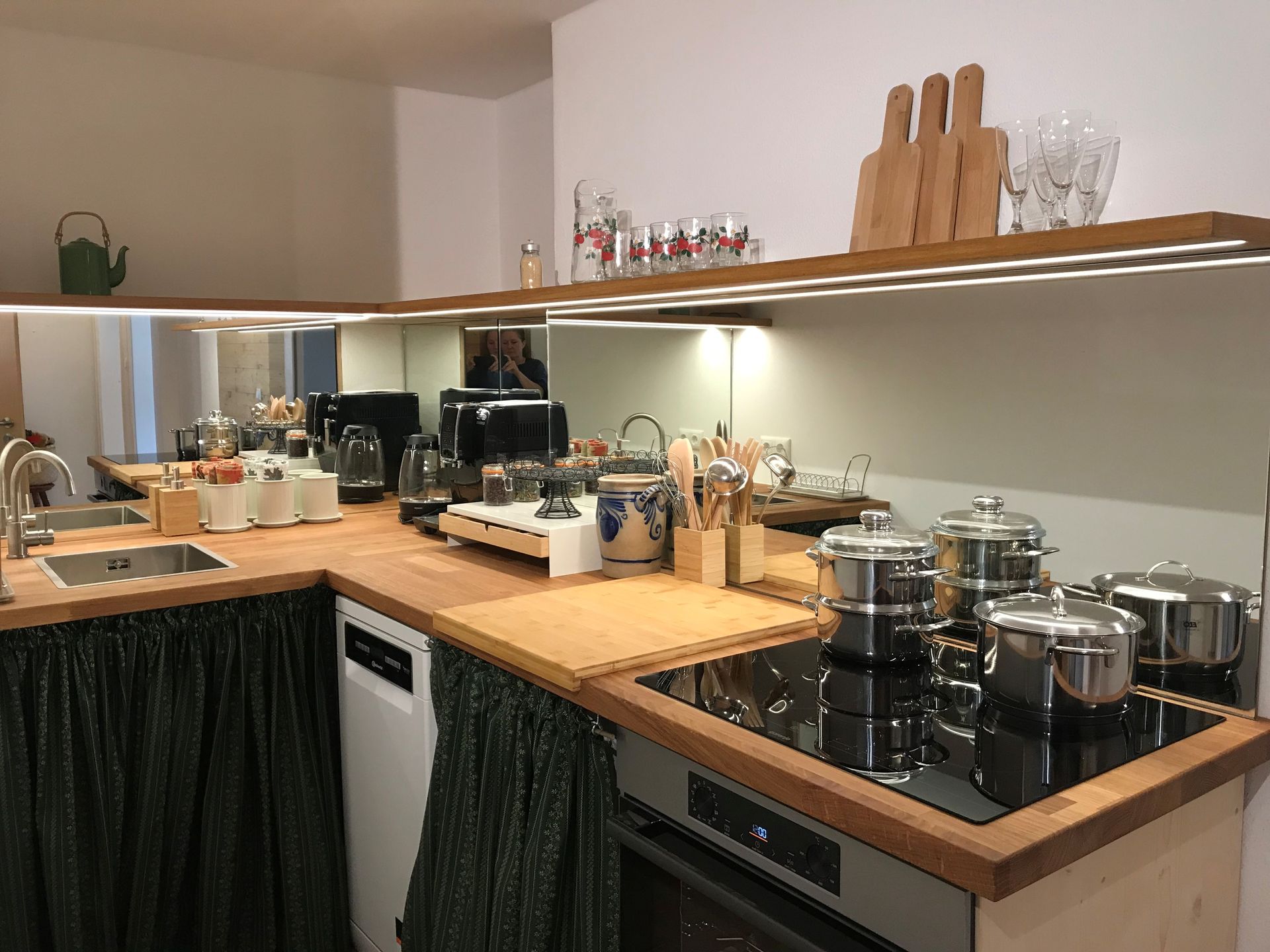 Küche mit Arbeitsplatten aus Holz, verspiegelter Rückwand und Töpfen und Geräten aus Edelstahl.