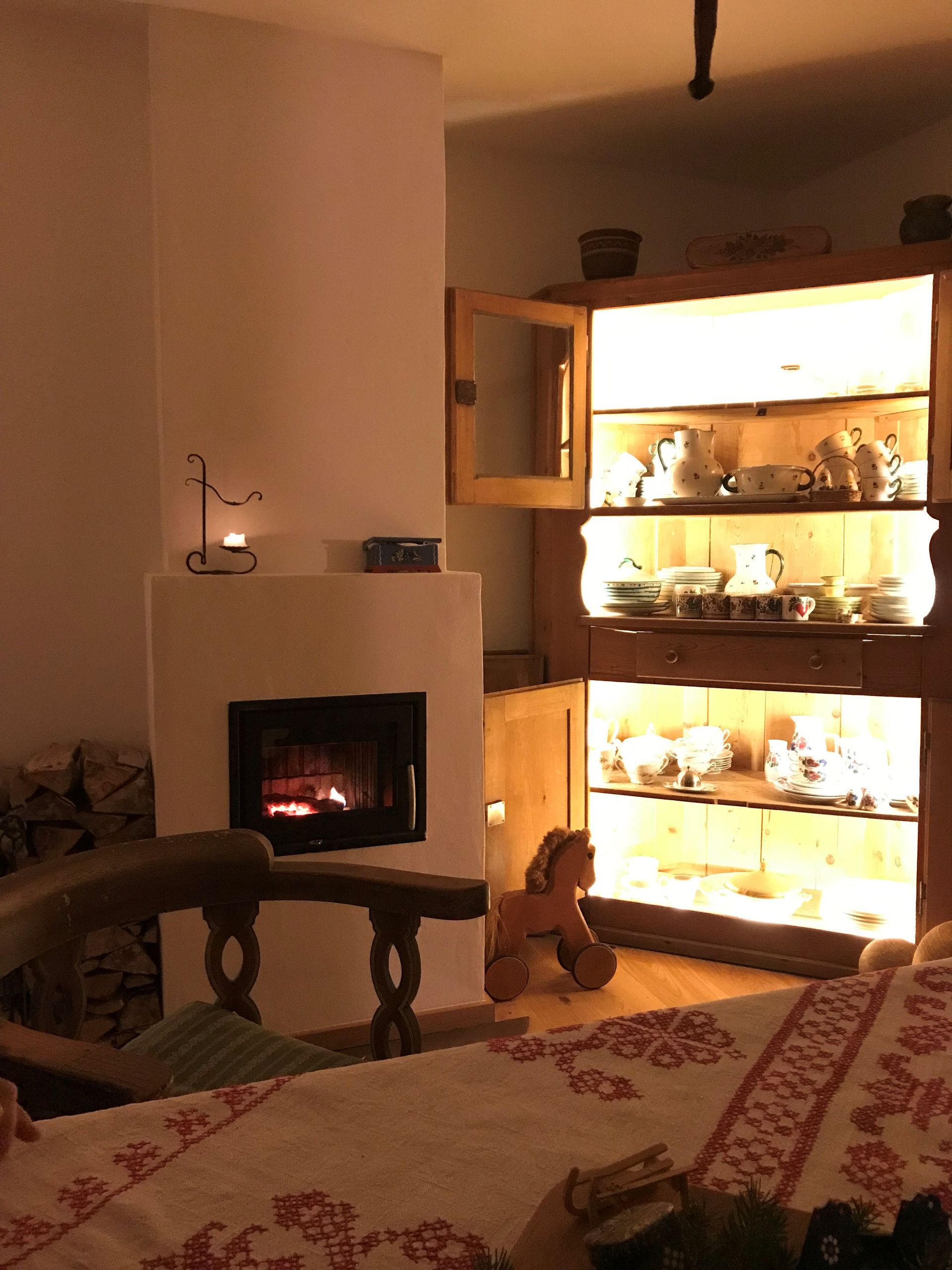 Gemütliches Zimmer mit brennendem Kamin, Holzschrank mit Geschirr und hölzernem Schaukelpferd.