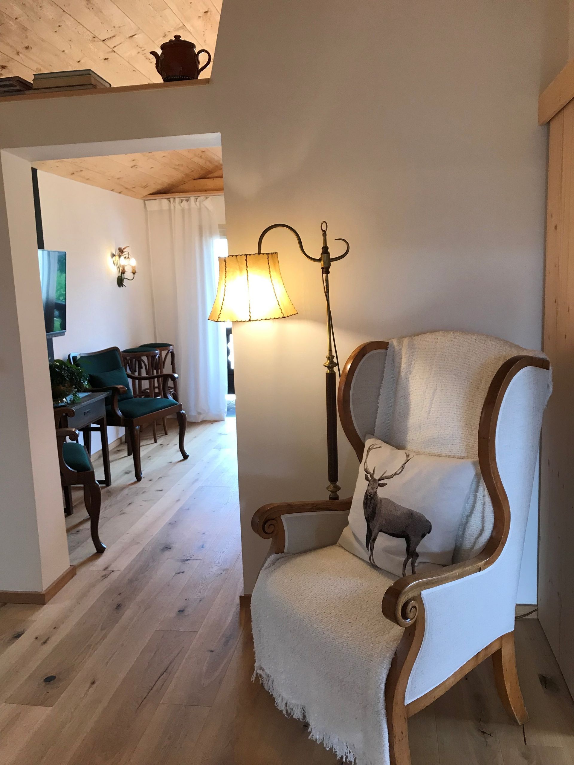 Gemütliches Interieur mit einem weißen Ohrensessel, einer Stehlampe und einer Tür zu einem Zimmer.