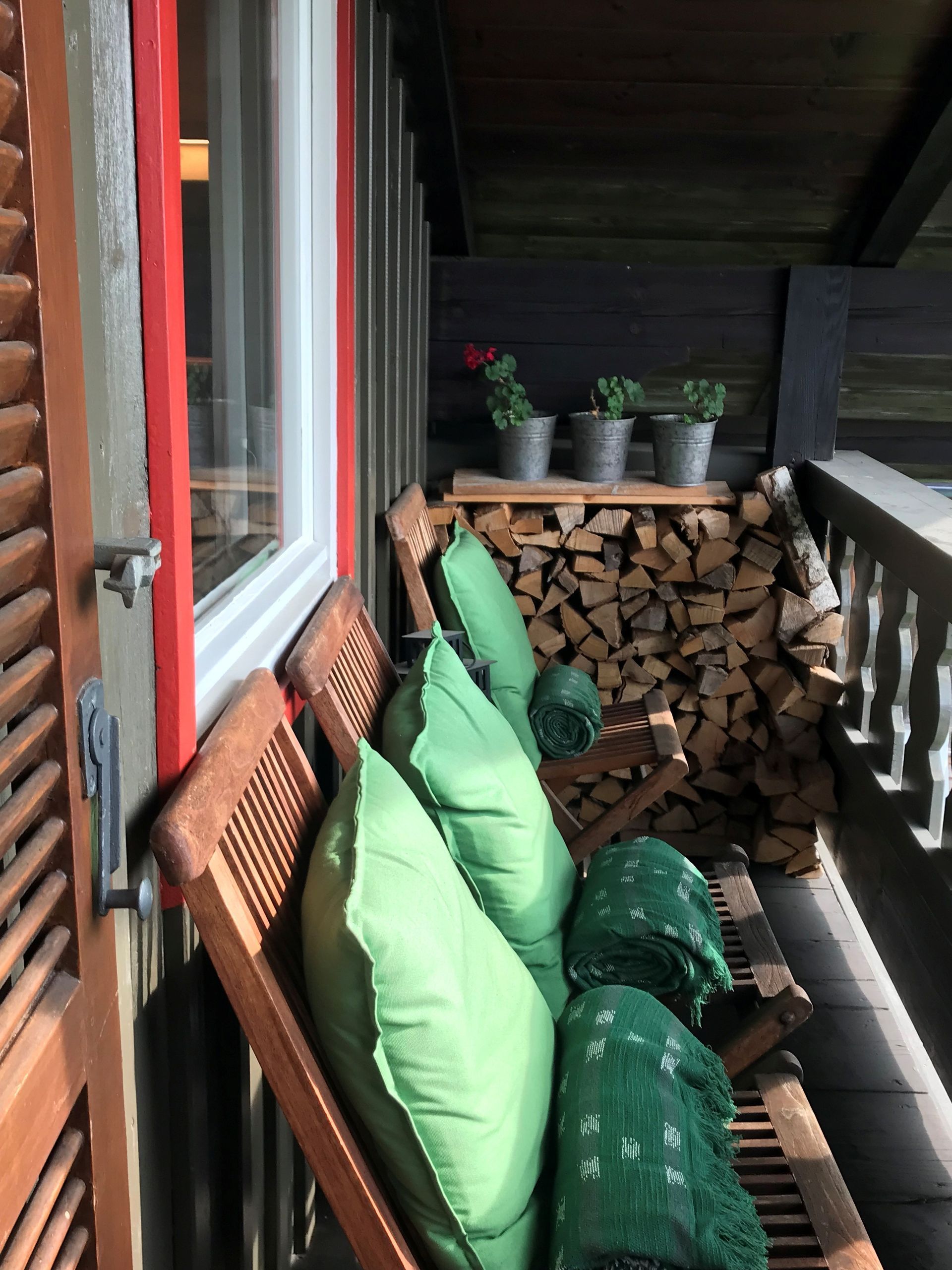 Balkon mit Holzstühlen und grünen Kissen, Brennholz und Topfpflanzen.