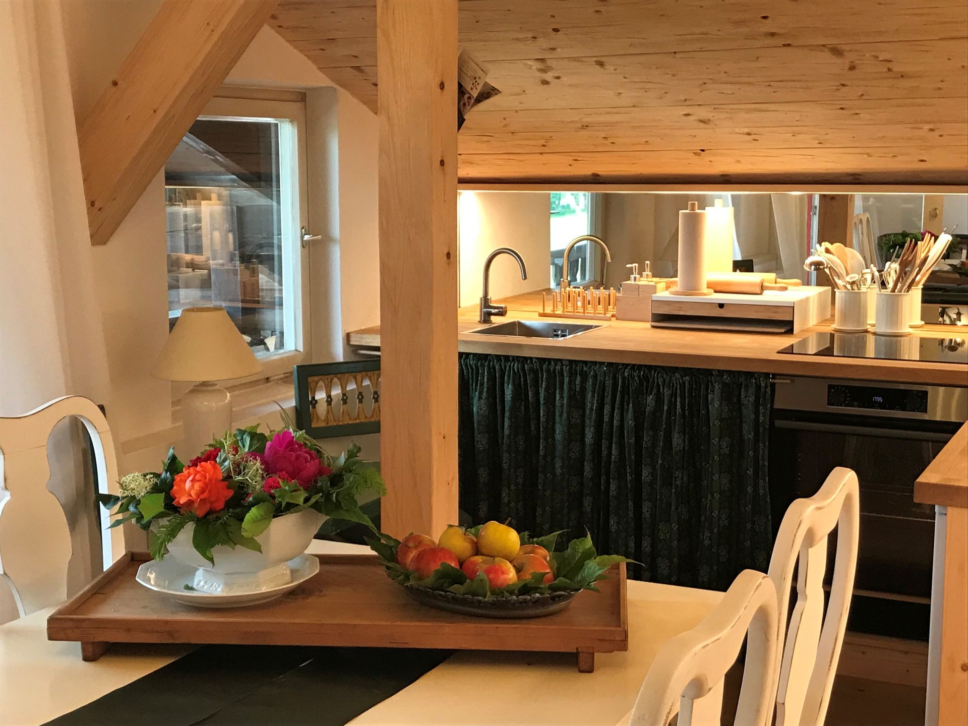 Ein mit Blumen und Obst gedeckter Esstisch führt zu einem kleinen Küchenbereich mit Spüle und Herd.