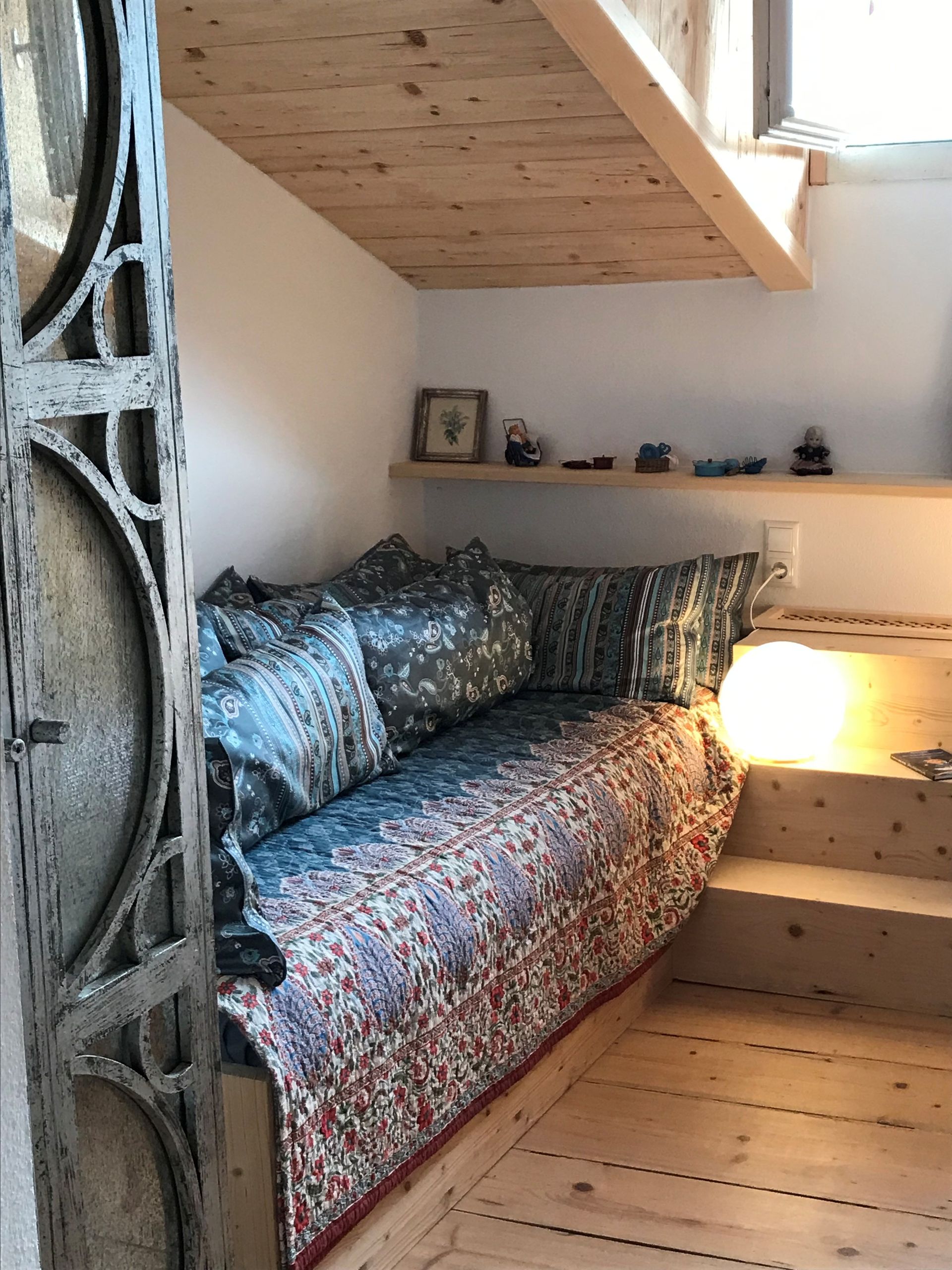 Gemütliche Ecke mit einem blumenbezogenen Tagesbett, Kissen und einer Holztreppe.