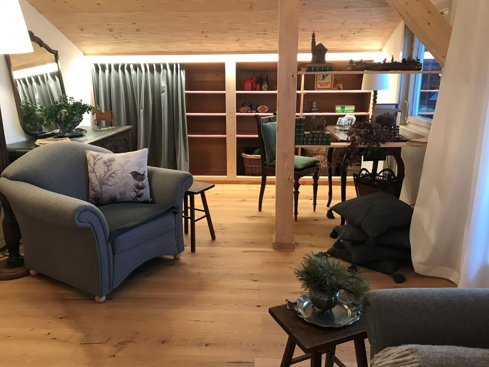 Wohnbereich mit hellem Holzboden, Einbauregalen, einem blauen Sessel und einem kleinen Tisch.