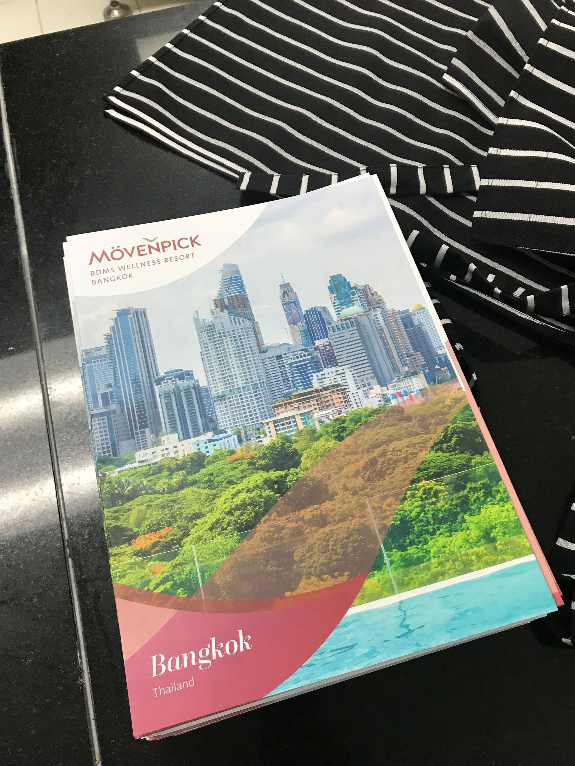 Broschüre für das Mövenpick Bangkok Hotel, mit einer Stadtkulisse und gestreiftem Stoff im Hintergrund.