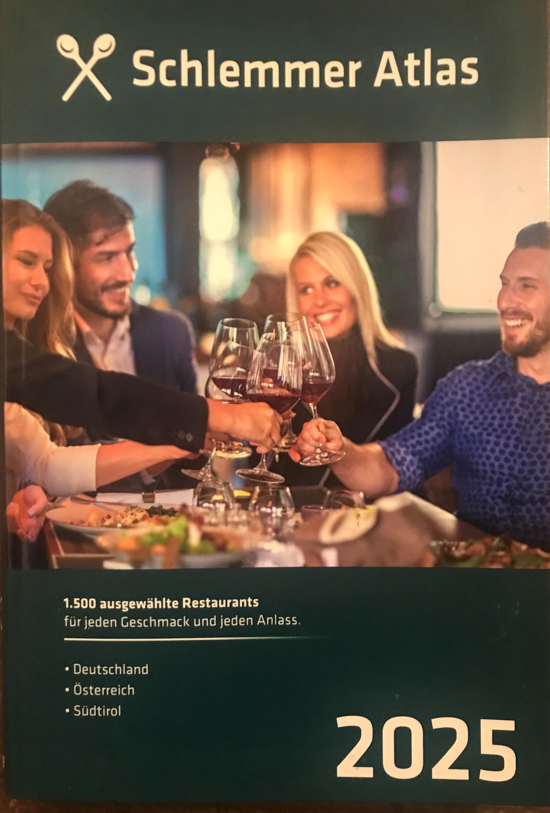 Buchcover „Schlemmer Atlas 2025“: Menschen stoßen in einem Restaurant mit Weingläsern an.