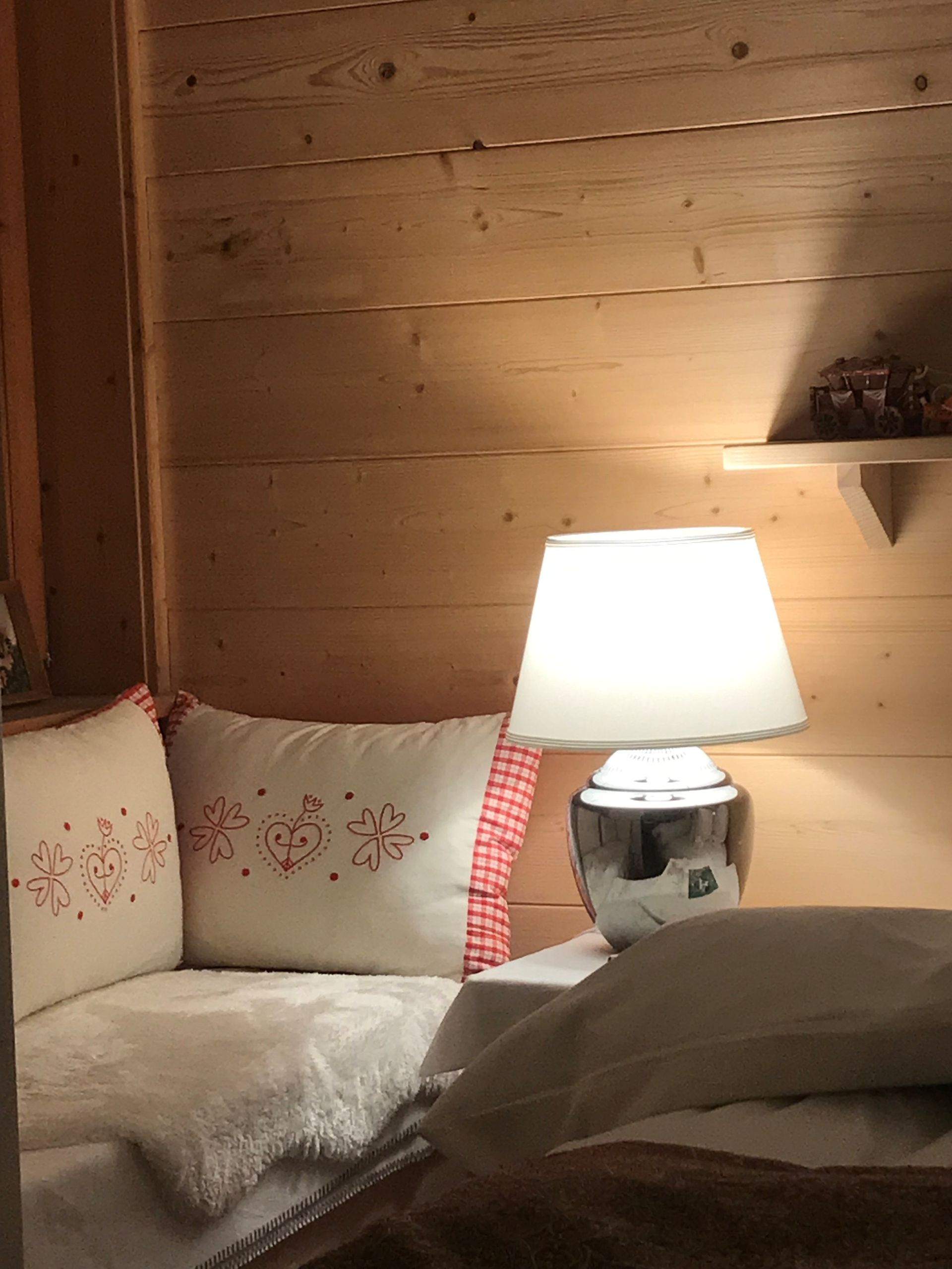 Gemütliche Hüttenecke mit beleuchteter Lampe auf dem Nachttisch, Kissen und Holzwänden.