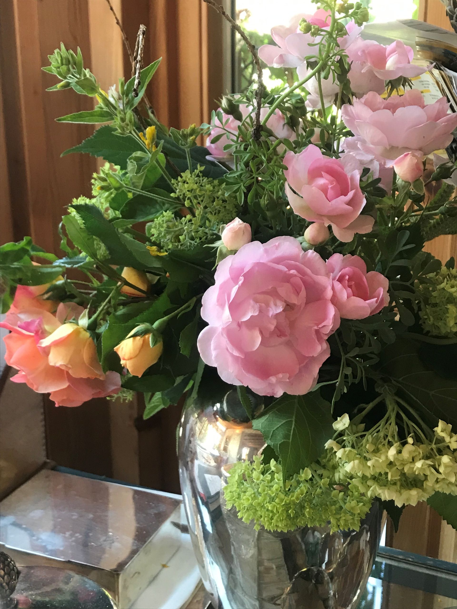 Rosa und gelbe Rosen in einer silbernen Vase mit üppigem Grün, im Innenbereich arrangiert.