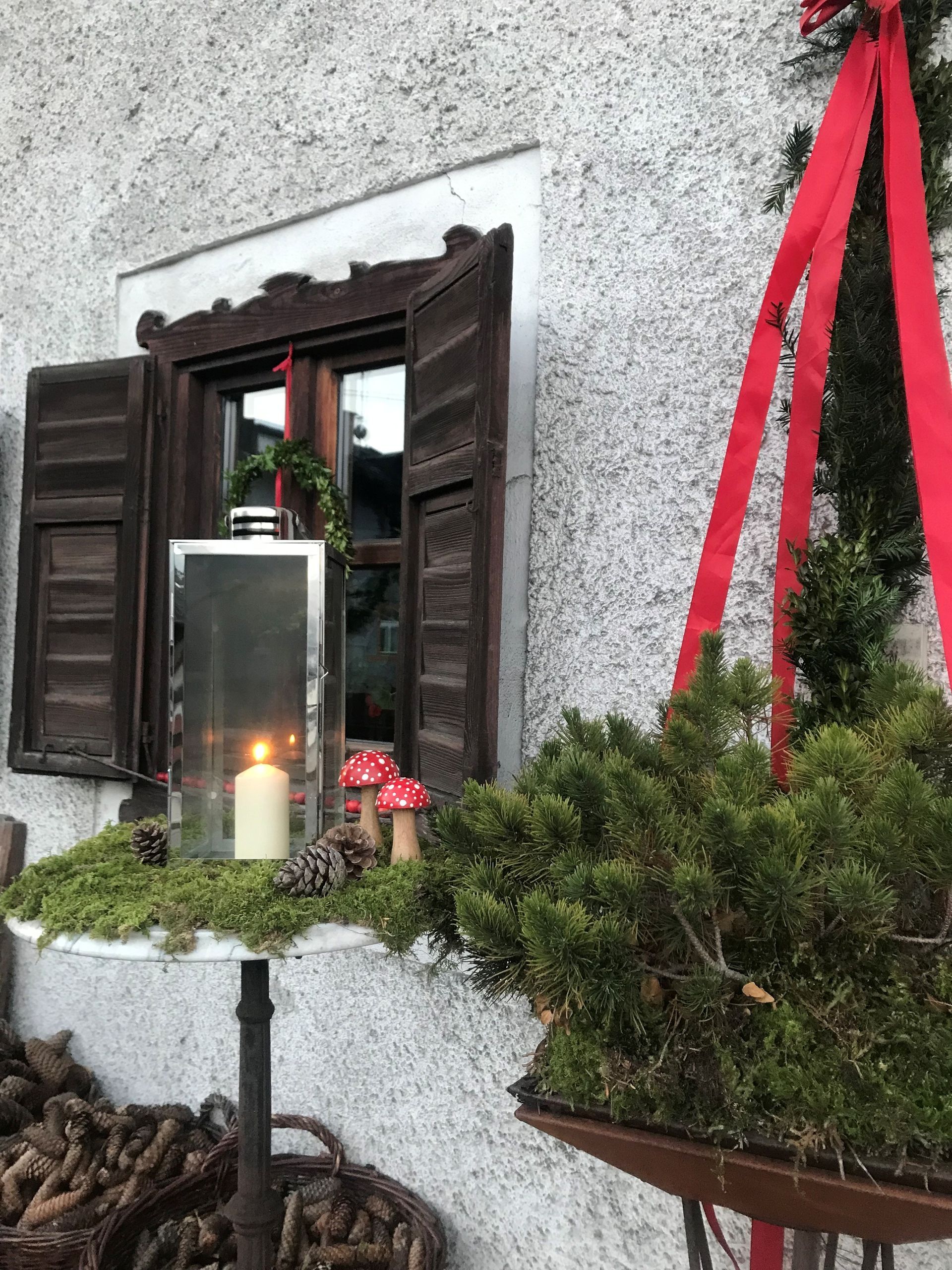 Fenster mit Fensterläden, brennende Kerze in einer Laterne und weihnachtliches Grün, rotes Band.